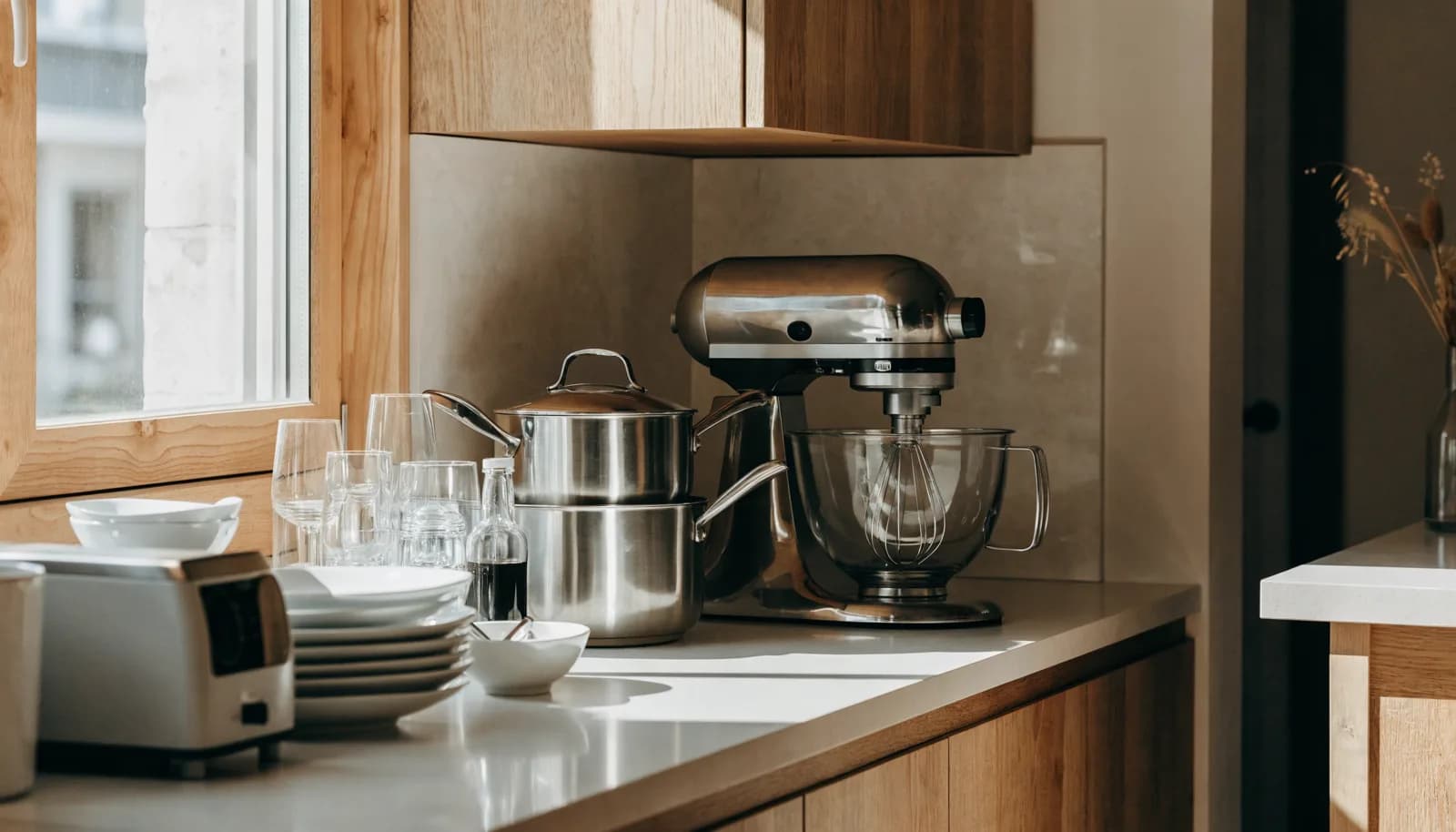 Bright kitchen counter arranged with a stand mixer, cookware, and stacked dishes