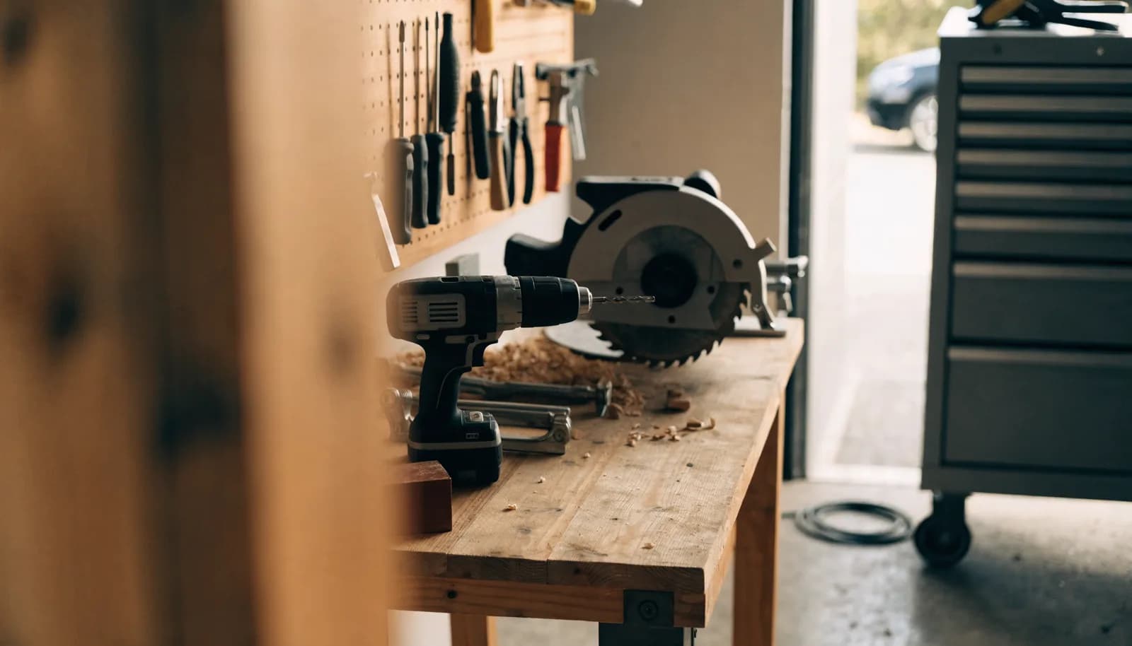 Tidy home garage workshop with a wooden workbench, a pegboard of hand tools, and a rolling tool chest in natural daylight